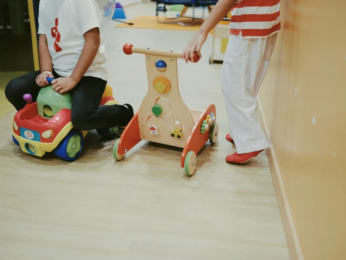 A toddler pushing a wooden walker toy along a hallway
