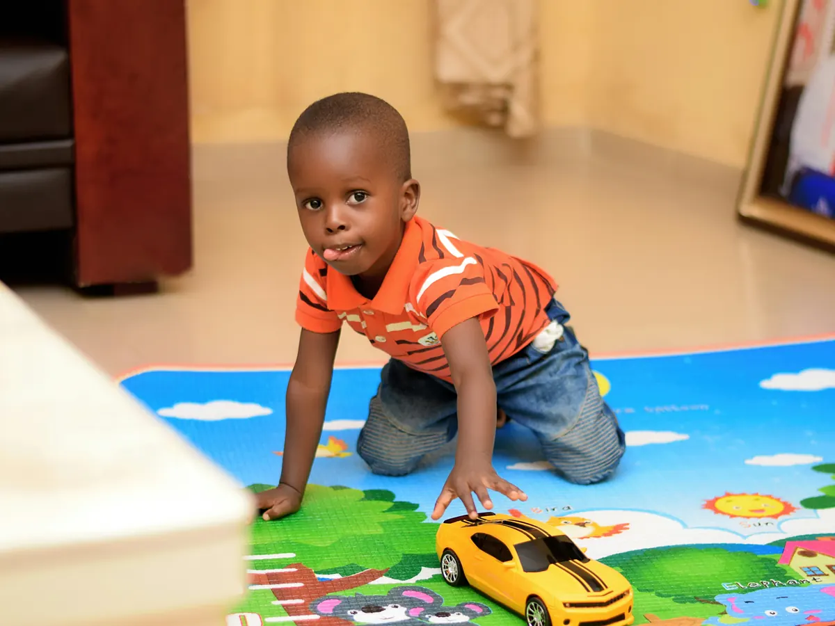 A child kneeling on a play mat pushing a toy car